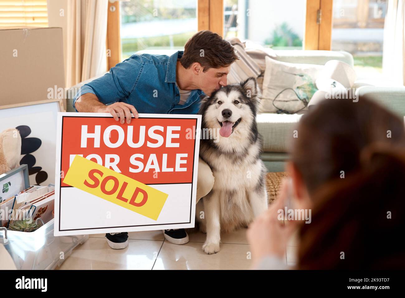 Wir waren glücklich mit unserem neuen Zuhause. Ein glückliches junges Paar und ihr Hund machten Fotos mit einem verkauften Schild in ihrem neuen Zuhause. Stockfoto