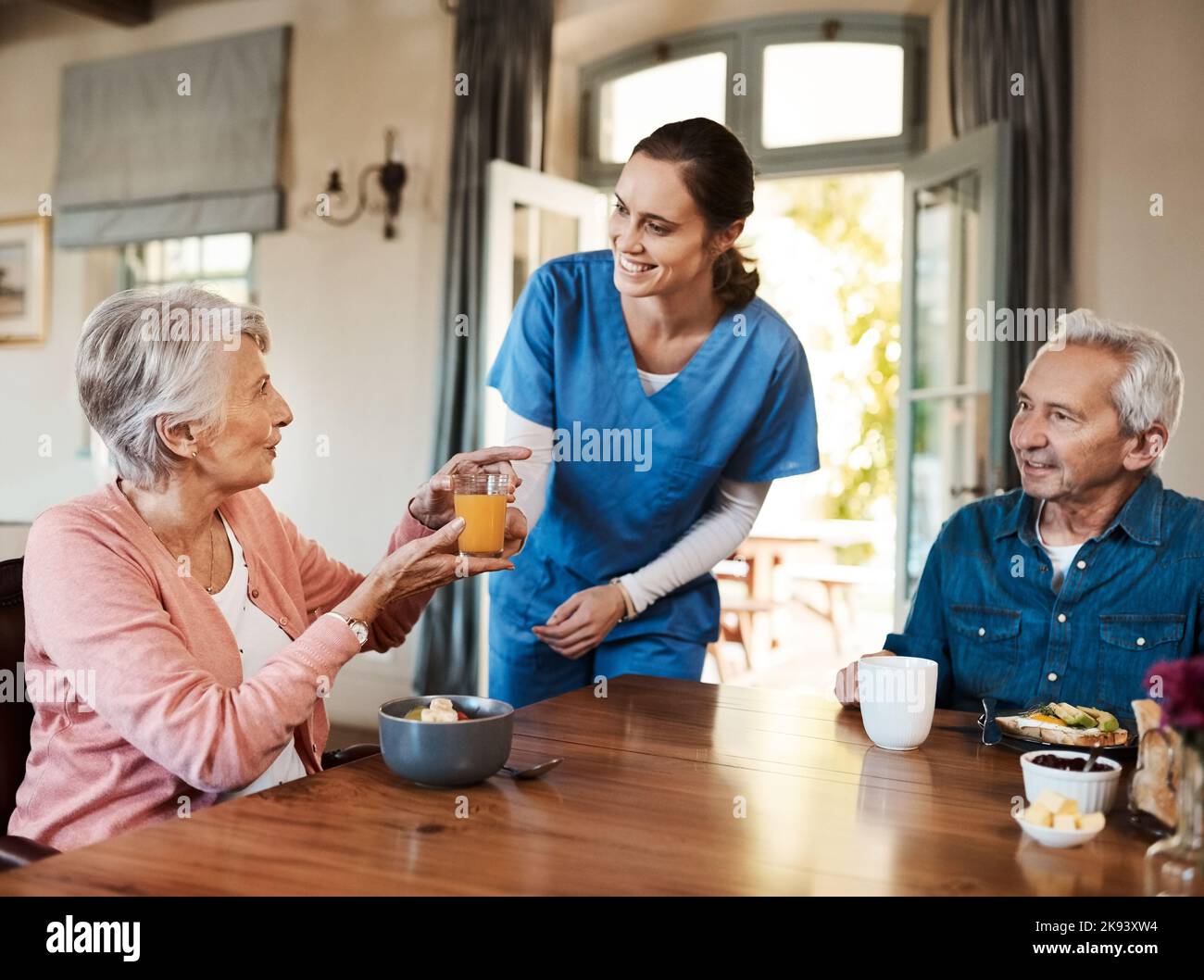 Es ist frisch gepresst, so wie man es mag. Eine junge Krankenschwester, die während des Frühstücks in einem Pflegeheim ein Seniorenpaar aufgesucht hat. Stockfoto