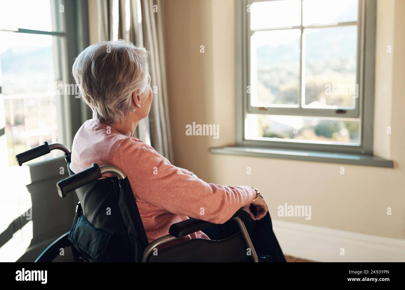 Wie ich wünschte, ich hätte mein Leben zurück. Eine ältere Frau im Rollstuhl schaute nachdenklich aus einem Fenster zu Hause. Stockfoto