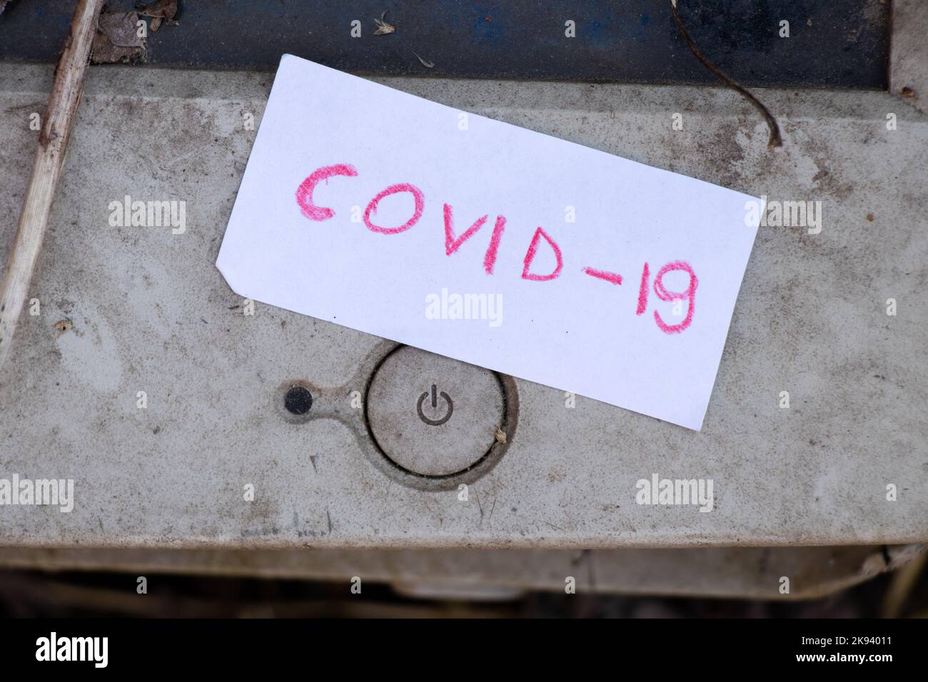 COVID-19 ist auf ein Stück Papier geschrieben und liegt neben dem Ausschaltknopf an einem Computer Stockfoto