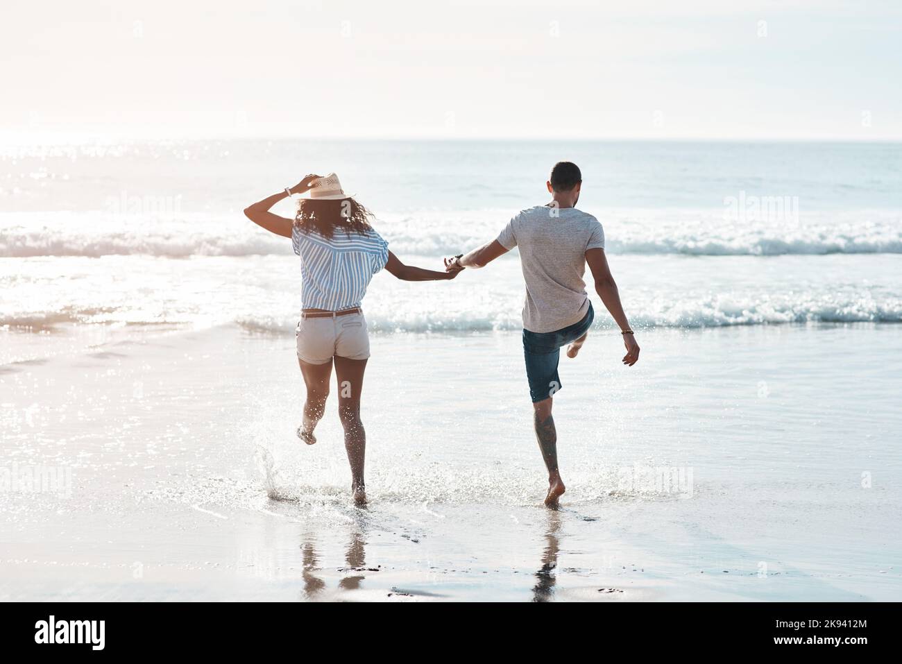 Die Stimmung des Sommers spüren. Rückansicht eines jungen Paares, das am Strand im Wasser planscht. Stockfoto