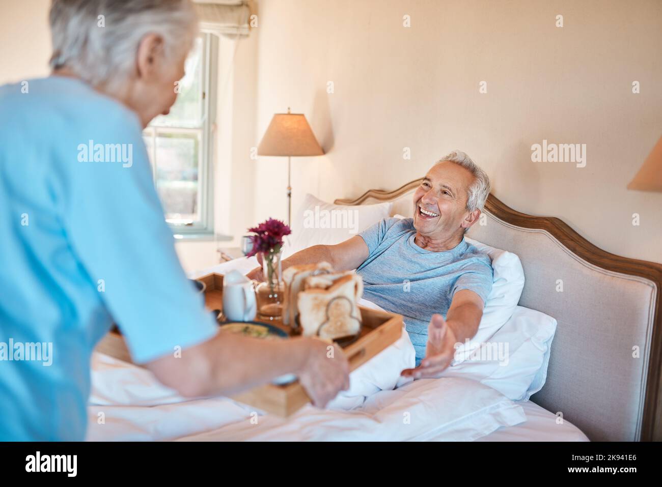 Das Frühstück ist fertig, meine Liebe. Eine ältere Frau serviert ihrem glücklichen Mann das Frühstück im Bett in ihrem Pflegeheim. Stockfoto