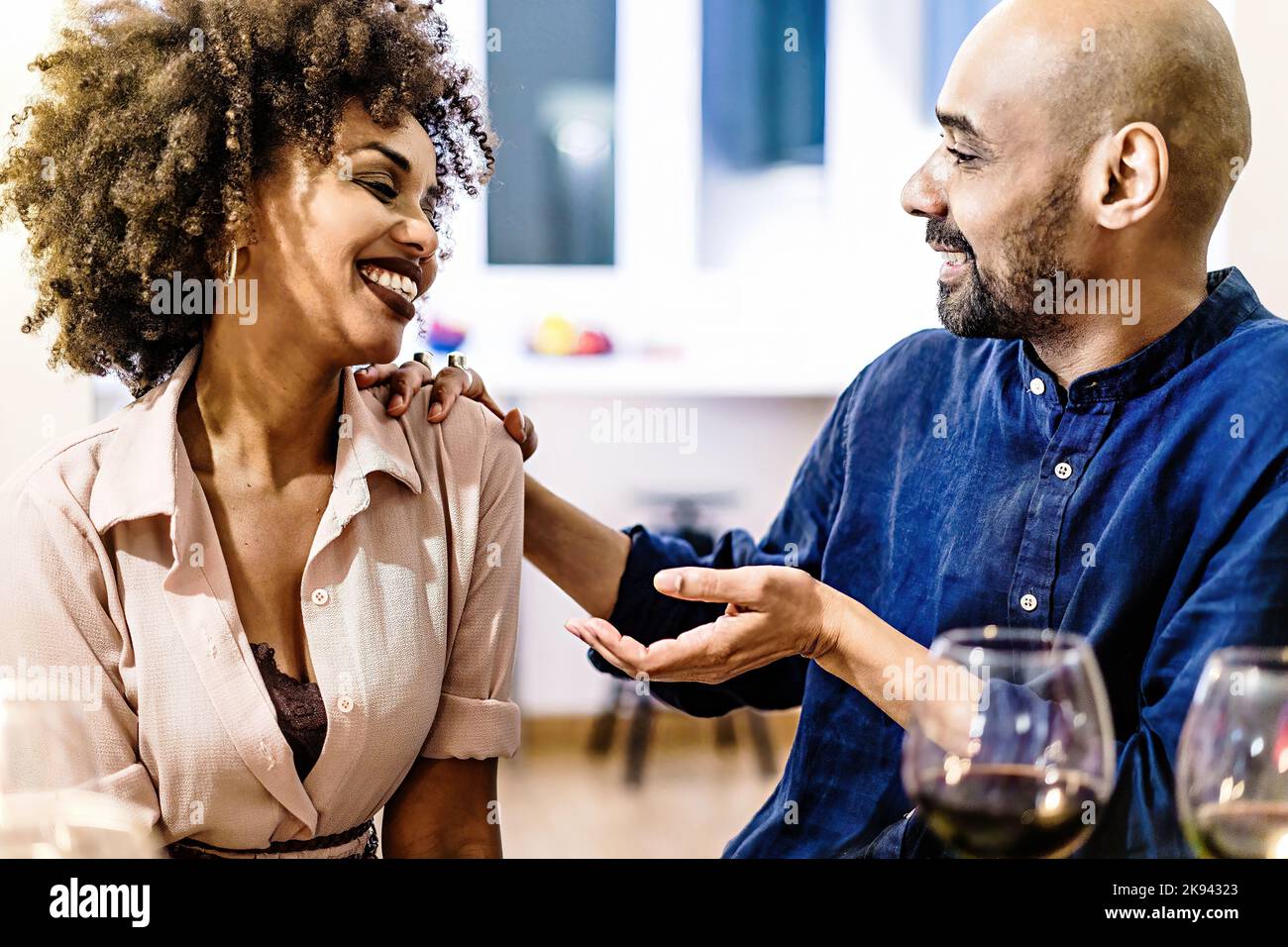 Glückliches multiethnisches erwachsenes Paar flirtet auf einem Tisch zu Hause sitzen Spaß miteinander reden Essen und Wein trinken - Menschen und Lebensstil concep Stockfoto