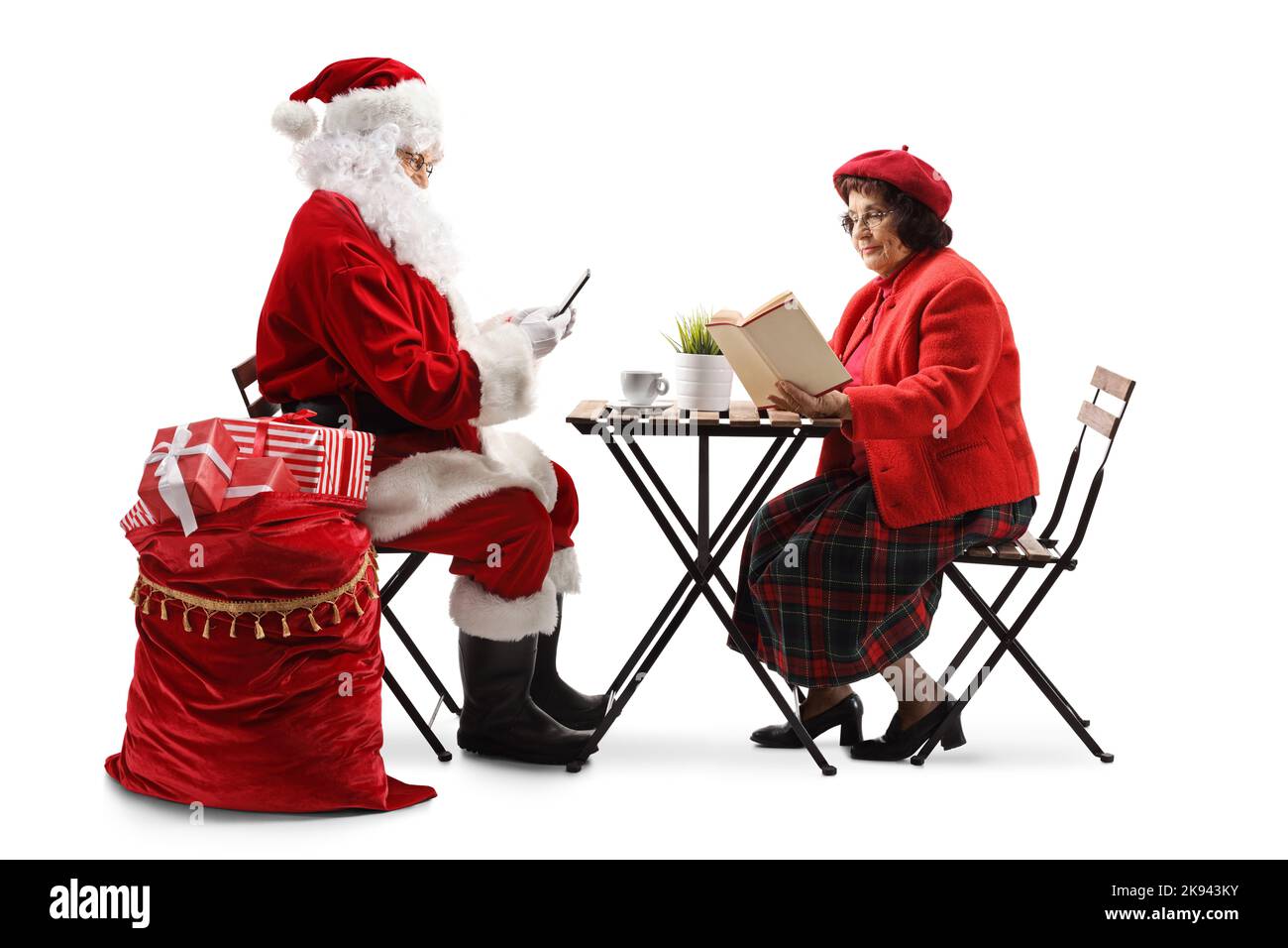 Weihnachtsmann mit Smartphone und einer älteren Frau, die an einem Tisch sitzt und auf weißem Hintergrund ein Buch liest Stockfoto