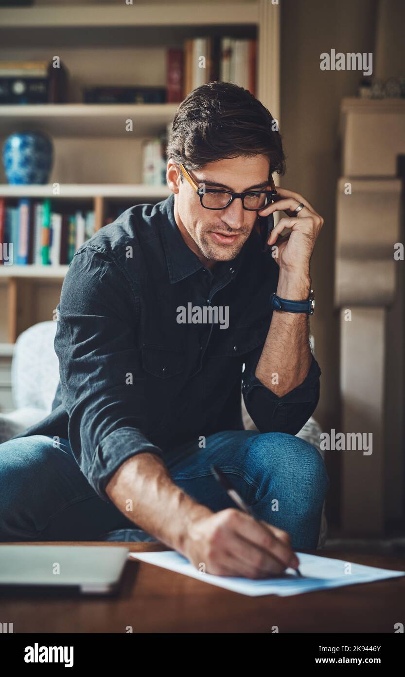 Jeder angehende Neuunternehmer muss lernen, wie man multitasking. Ein hübscher junger Geschäftsmann, der einen Anruf macht, während er in seinem Büro zu Hause arbeitet. Stockfoto
