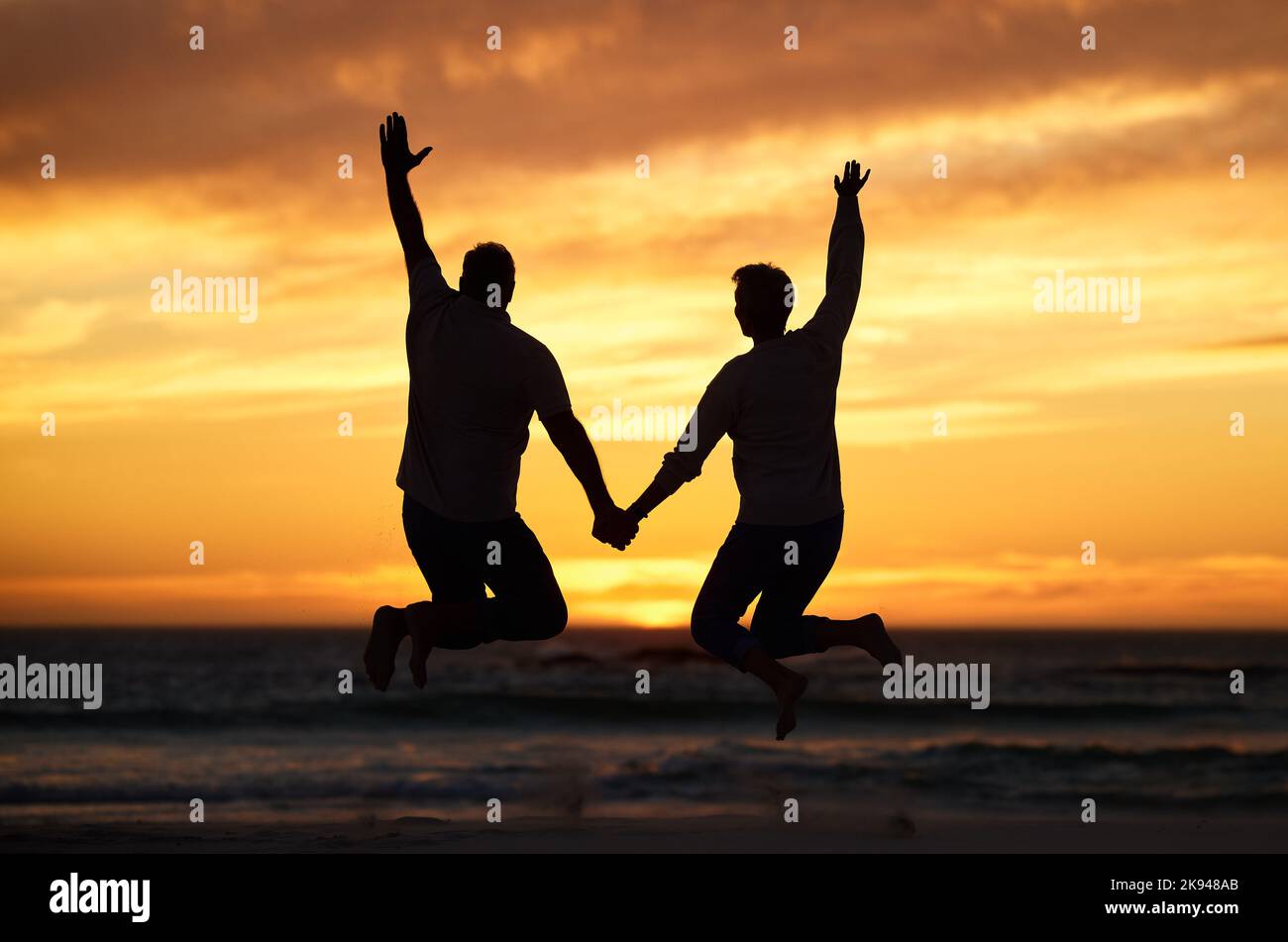 Paar, Sonnenuntergang und springen am Strand, während die Hände für Glück, Bindung oder Romantik im Urlaub halten. Menschen, lieben und glücklich auf See, Meer oder Dämmerung hinein Stockfoto