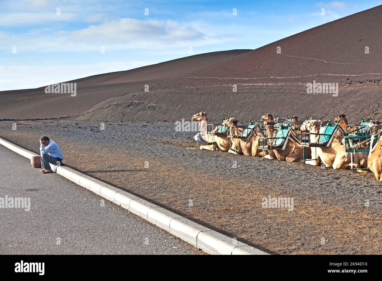 TIMANFAYA, SPANIEN - 2. JANUAR 2010: Kamelführer warten auf Touristen in Timanfaya, Spanien. Die Kamele gehören zum Dorf UGA und der Kamelreiter von UGA hav Stockfoto TIMANFAYA, SPANIEN - 2. JANUAR 2010: Kamelführer warten auf Touristen in Timanfaya, Spanien. Die Kamele gehören zum Dorf UGA und der Kamelreiter von UGA hav Stockfoto