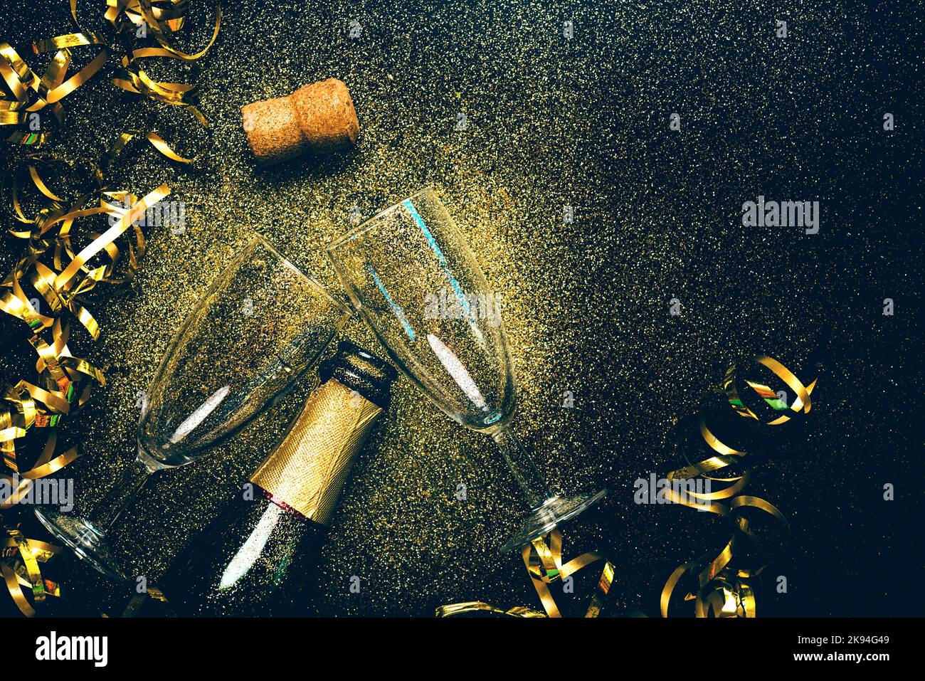 Frohes neues Jahr. Champagnerflasche mit zwei Gläsern, goldenen Luftschlangen und funkelndem Glitzer mit Kopierraum auf schwarzem Hintergrund. Silvesterfeier Stockfoto