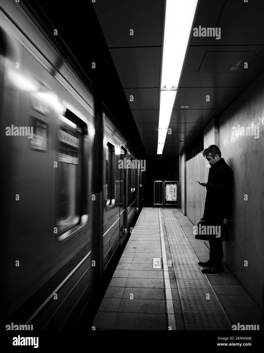 Eine Graustufenaufnahme eines Mannes, der auf die Ankunft des Zuges am Hauptbahnhof von Osaka wartet Stockfoto