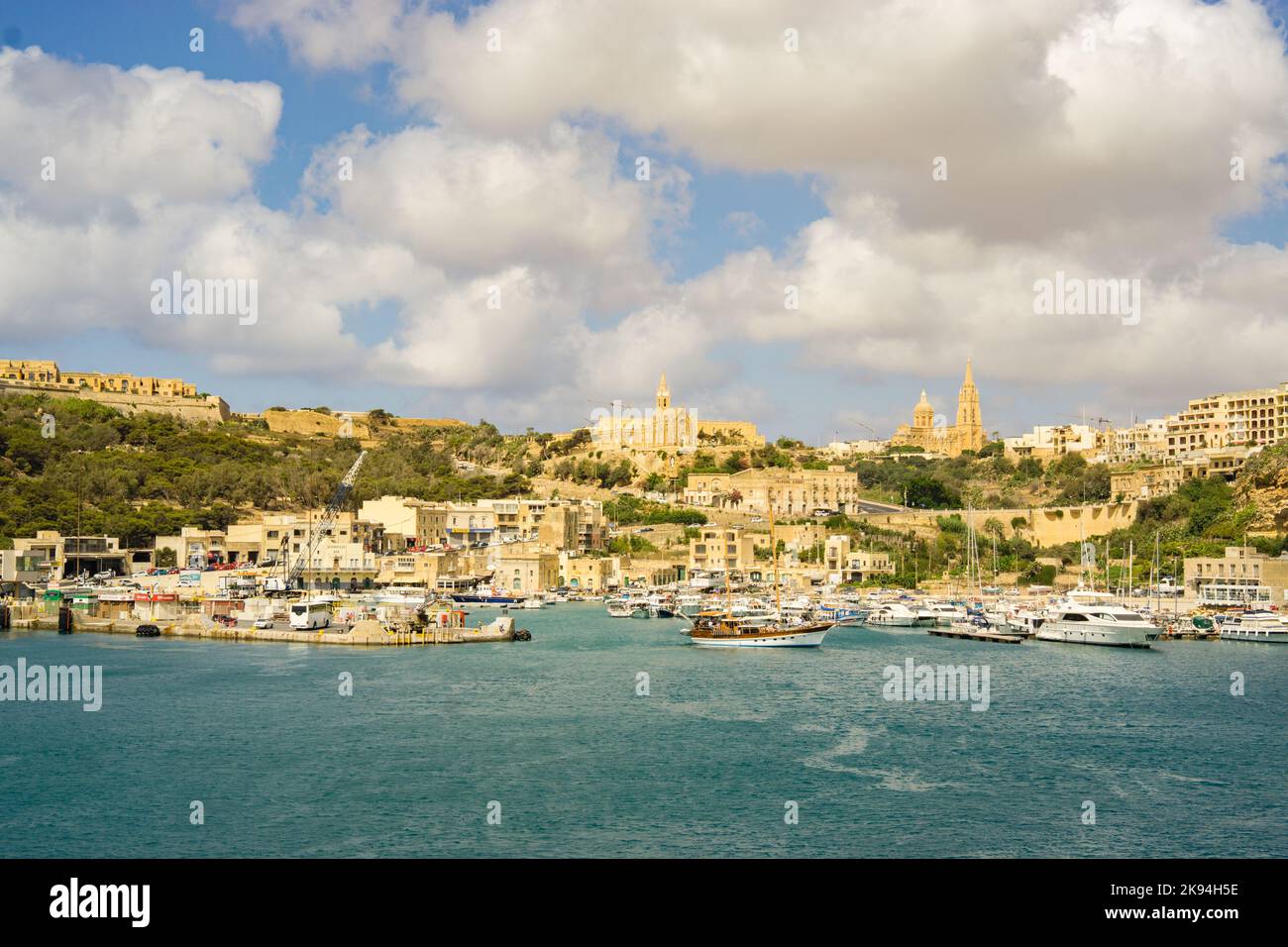 Der Hafen von Gozo mit Booten und die Stadt im Hintergrund unter einem bewölkten Himmel. Stockfoto