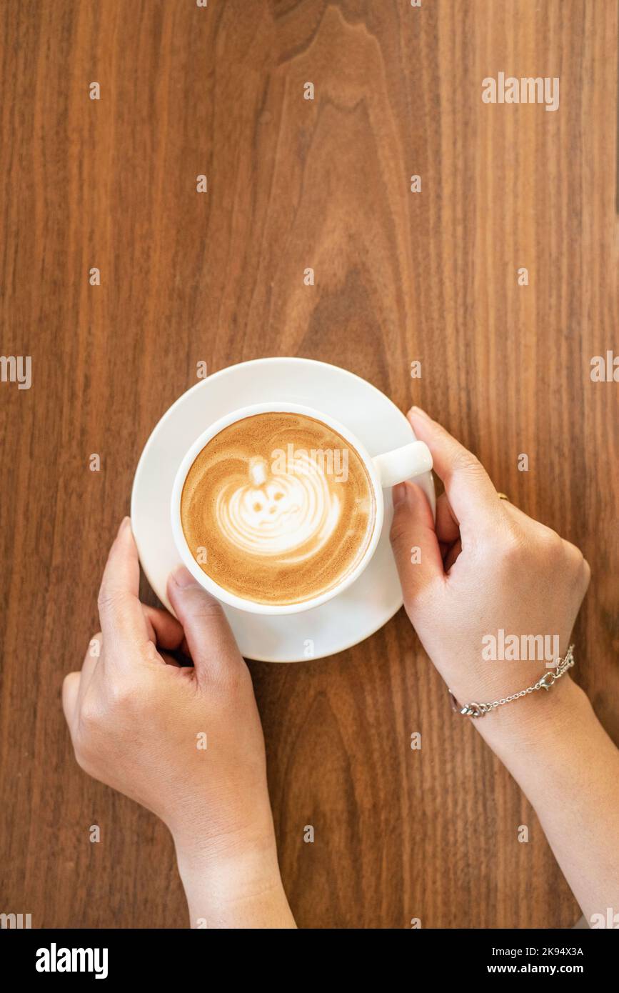 Halloween Kürbis Latte Kunst mit Hand auf Holztisch Stockfoto