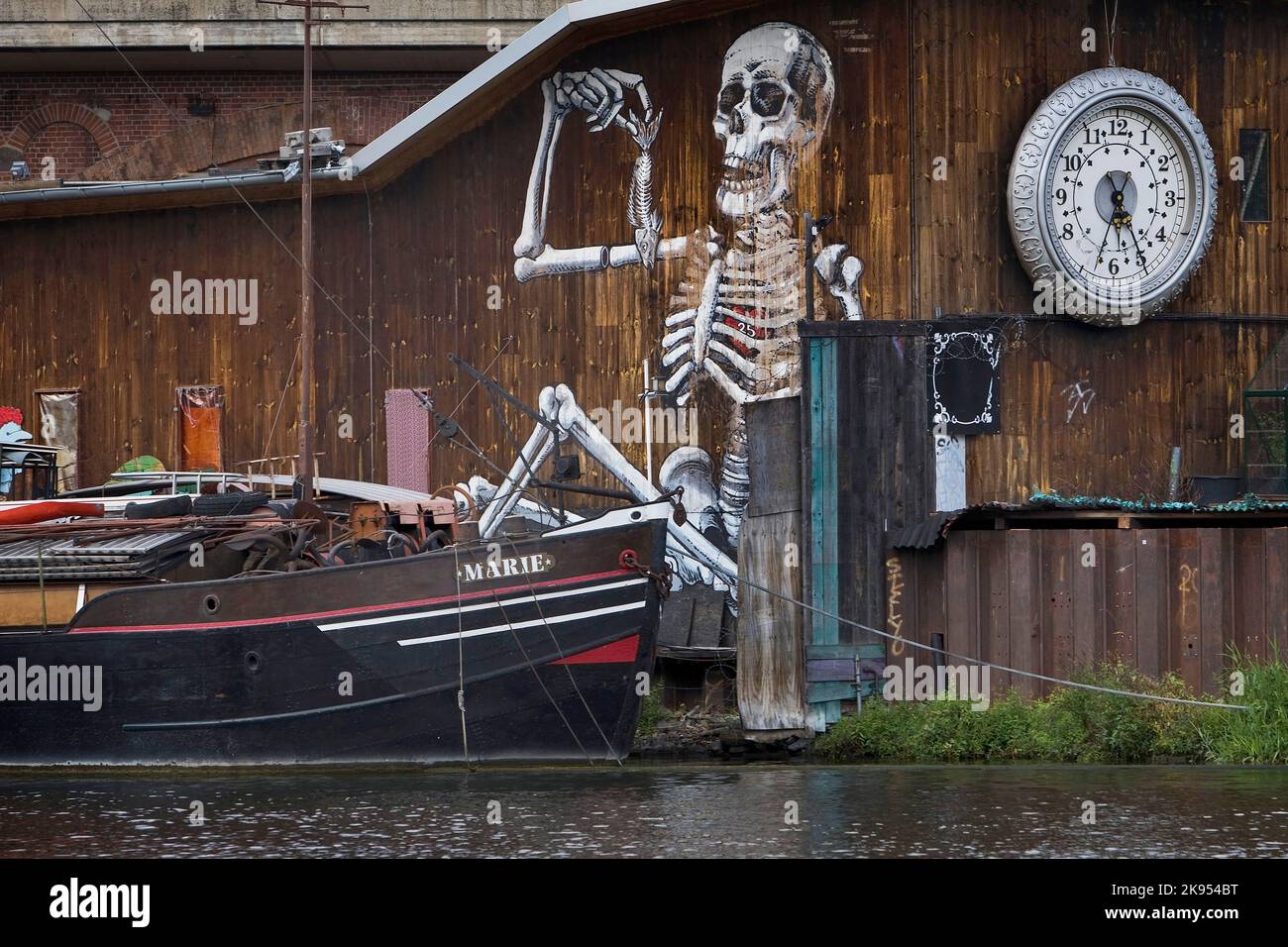 Holzwand mit Uhr und bemaltem Skelett auf der Spree mit Schiff bei der Michaelbrücke, Deutschland, Friedrichshain, Berlin Stockfoto