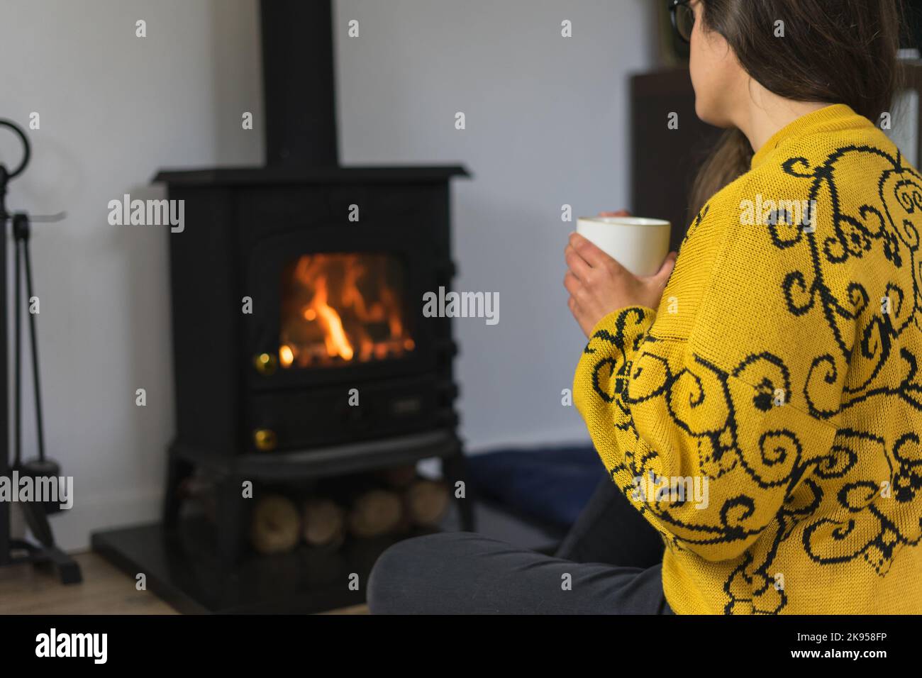 Frau hält eine Tasse heißes Getränk vor einem Kamin Stockfoto