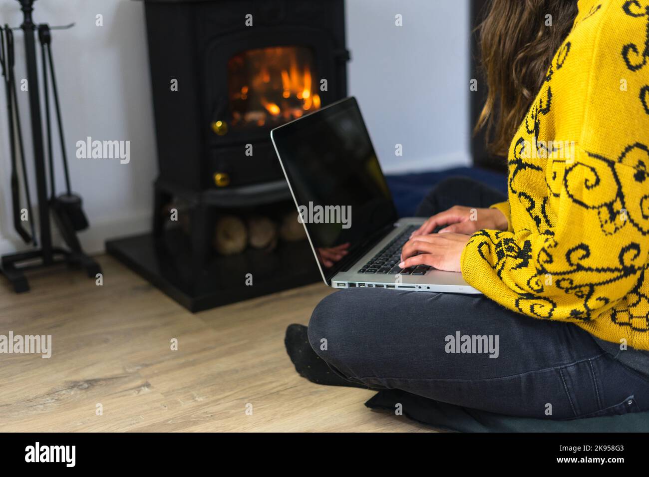 Frau, die vor einem Salamander oder Lagerfeuer auf ihrem Laptop arbeitet. Stockfoto