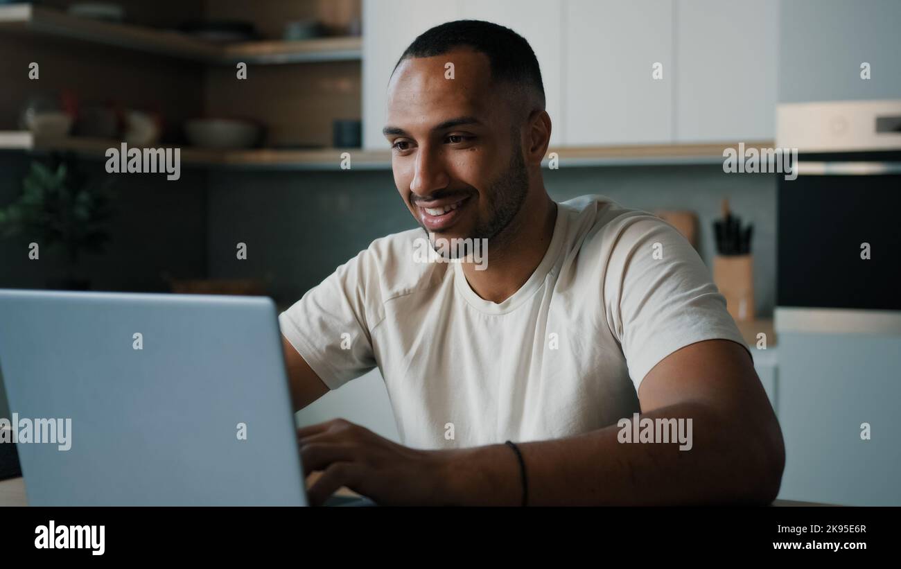 Afrikanischer Latina männlicher Mann in der Küche zu Hause online spielen Spiel Surfen im Netz Wette arbeiten Remote mit Laptop Einkaufen im Internet-Shop Bestellung Lieferung Stockfoto