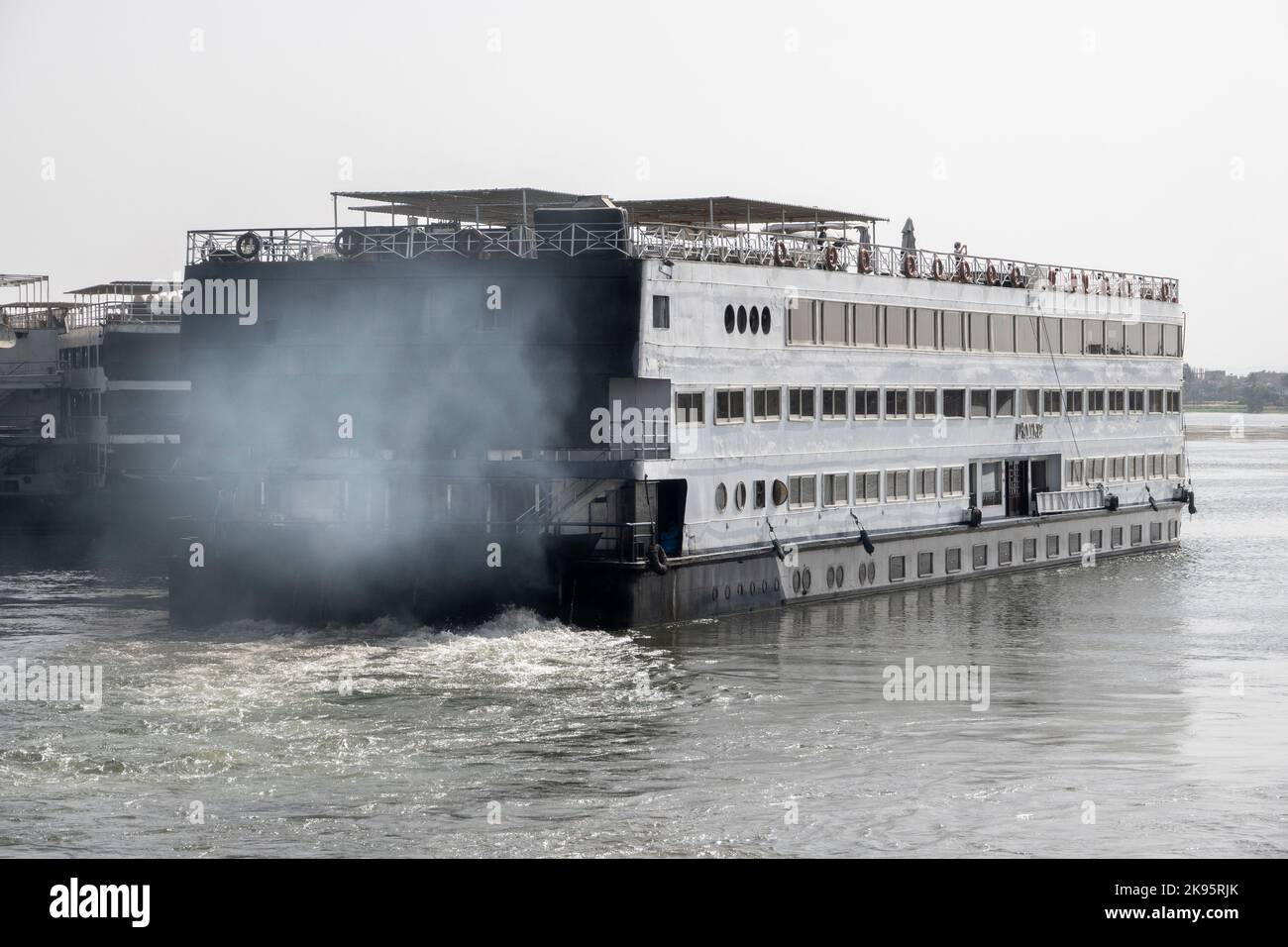 Ein festgeganntes Nilkreuzfahrtschiff, das in einem Dunst der Abgasverschmutzung vom Dock abfährt Stockfoto