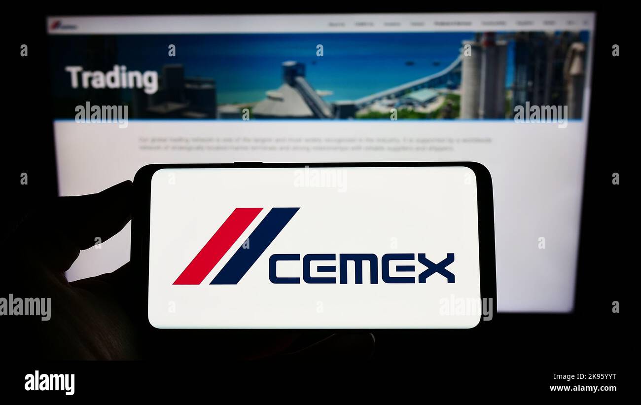 Person mit Mobiltelefon und Logo des mexikanischen Materialunternehmens CEMEX SAB de CV auf dem Bildschirm vor der Business-Webseite. Konzentrieren Sie sich auf die Telefonanzeige. Stockfoto