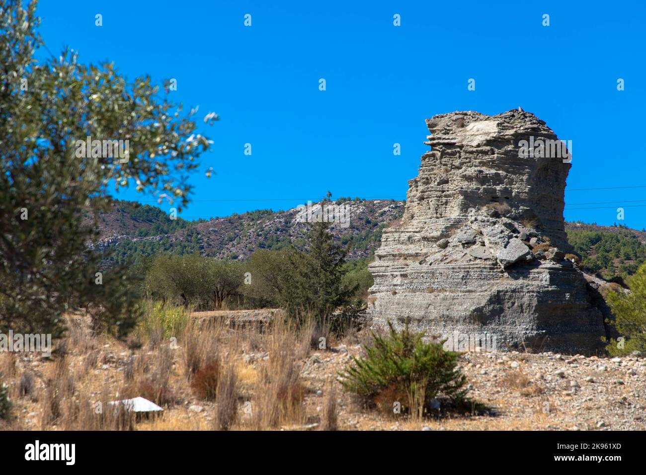 Olivenbäume mit großem Felsen und blauem Himmel im Hintergrund. Typisch griechische Landschaft. Tourismus- und Urlaubskonzept. Stockfoto