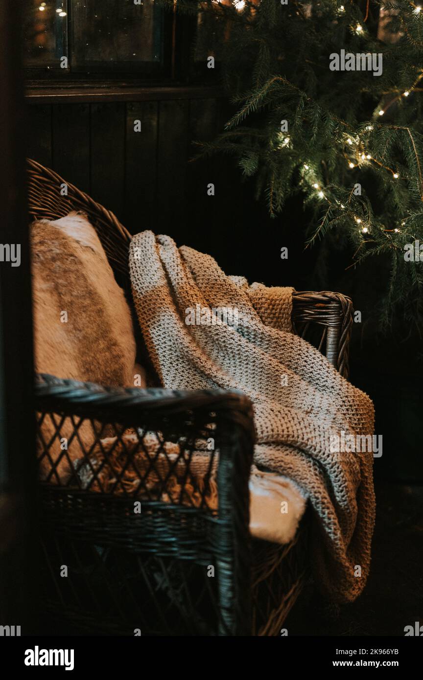 weihnachten und Neujahr. Gemütlicher Sessel oder Korbstuhl mit einem bequemen gestrickten Karree und einem Pelzkissen in der Nähe eines geschmückten weihnachtsbaums mit g Stockfoto