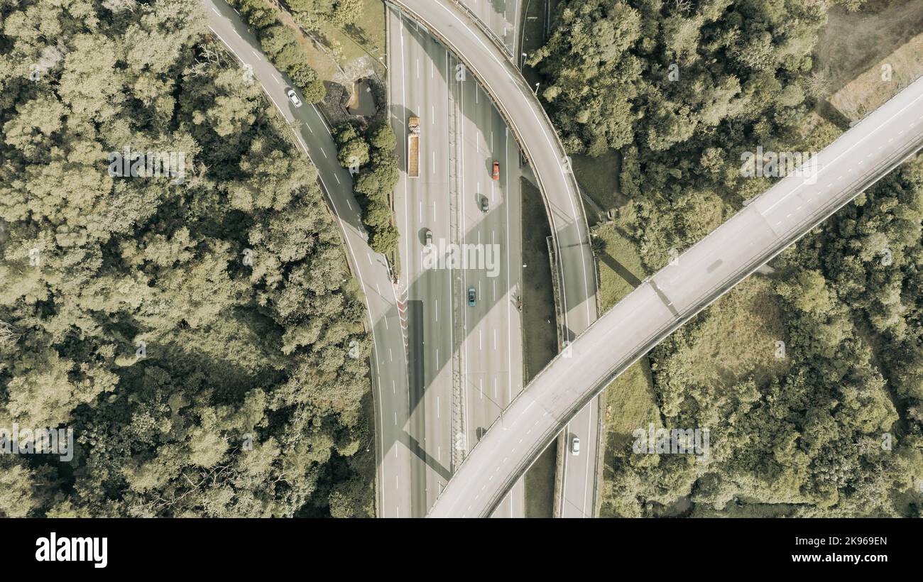 Luftaufnahme direkt über einer sechsspurigen Autobahn. Blick von oben auf Asphaltstraße führt durch das Feld und Wald. Antenne. Limousine Autos fahren auf der Autobahn Stockfoto