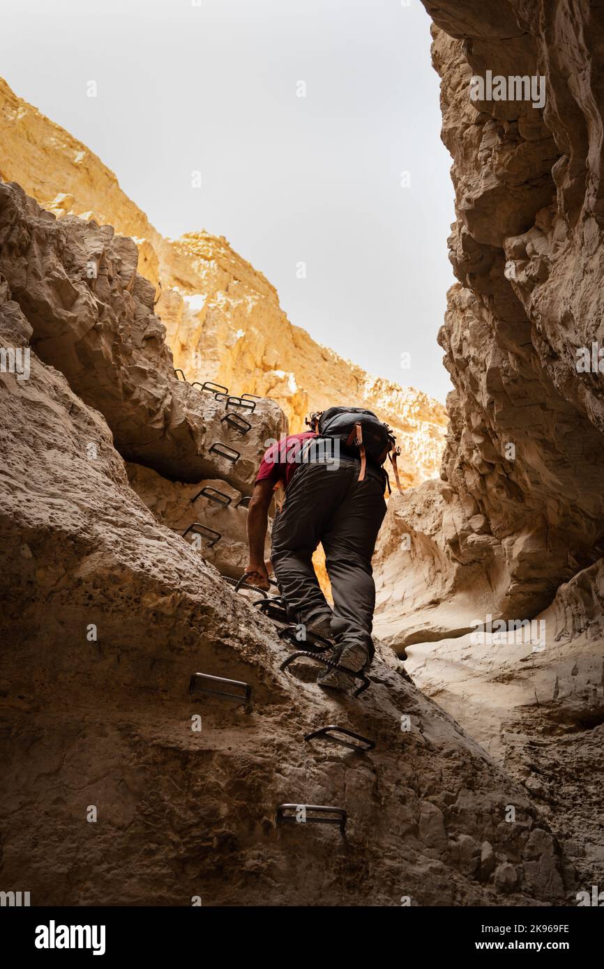 Wanderer, die Sprossen benutzen, um auf einem Felsen in einem Wüstenschlucht zu klettern Stockfoto