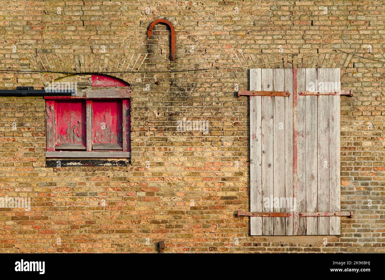 Verzweifeltes und abgenutztes Fenster mit Fensterläden und Backsteintür an der Seite des Quay Old Warehouse Wharf. King's Lynn UK Stockfoto