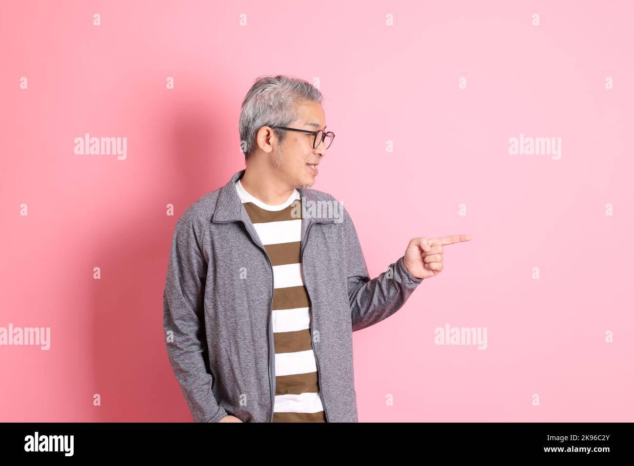 Der 40s-jährige asiatische Mann, der auf dem rosa Hintergrund mit legerer Kleidung stadiert. Stockfoto