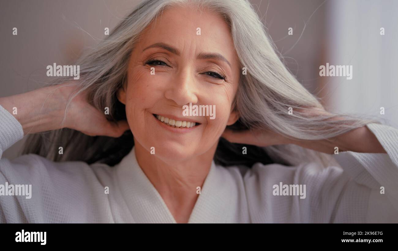 Wunderschöne schöne 60s alten mittleren Alters reifen kaukasischen Frau Oma älter 50s Dame lächelnd Blick auf die Kamera zu Hause Verwöhnung berühren grau Stockfoto