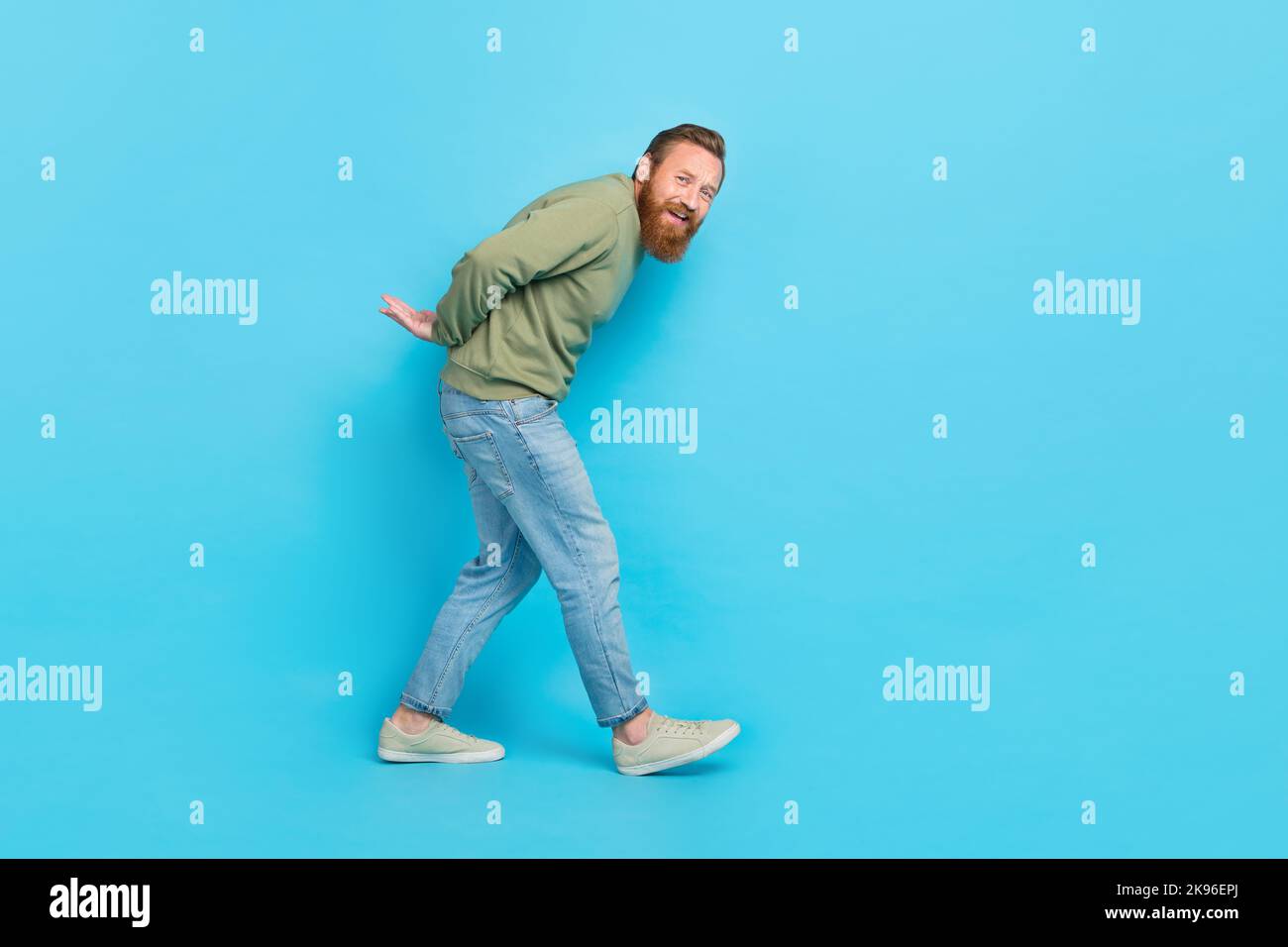 Foto in voller Größe von lustig aufgeregt Mann mit roten Frisur gekleidet khaki Pullover halten Sie die Arme hinter dem Rücken isoliert auf blauem Hintergrund Stockfoto