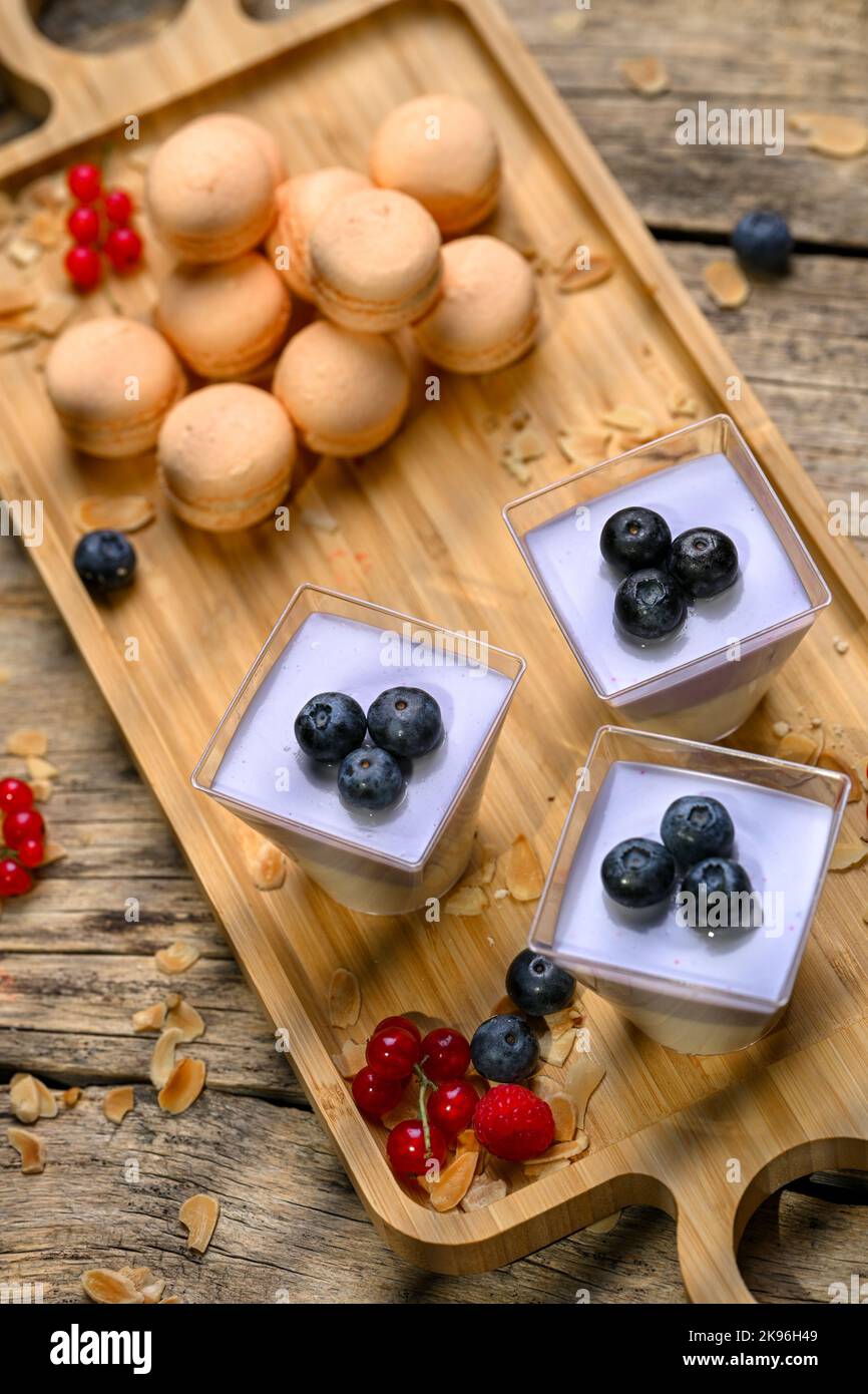 Ein schöner Schuss von weißem und violettem Mousse mit Heidelbeeren und Makronen auf einem Holzbrett Stockfoto