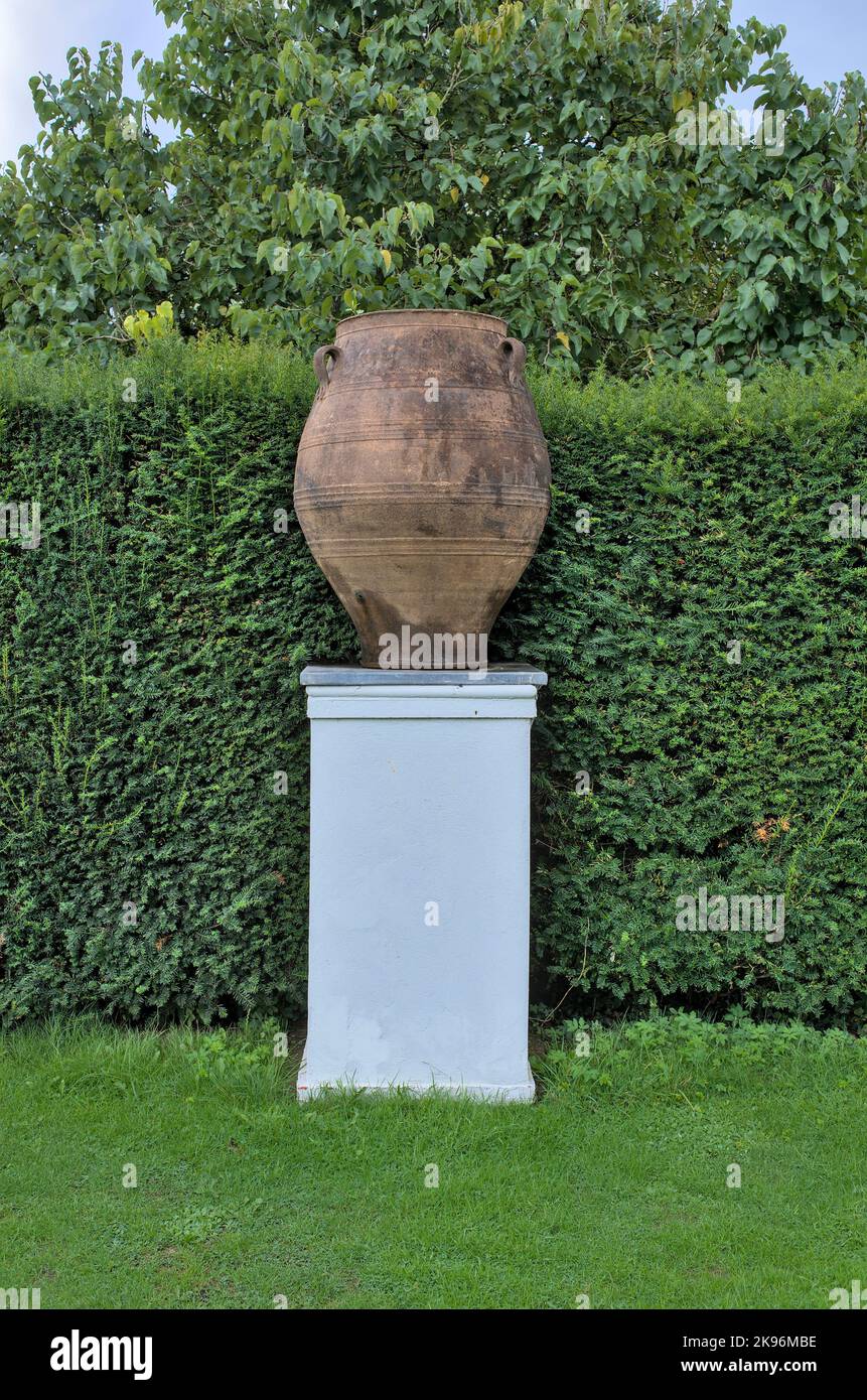 Große Terrakotta-Urne auf weißem Sockel - Hecke im Hintergrund Stockfoto