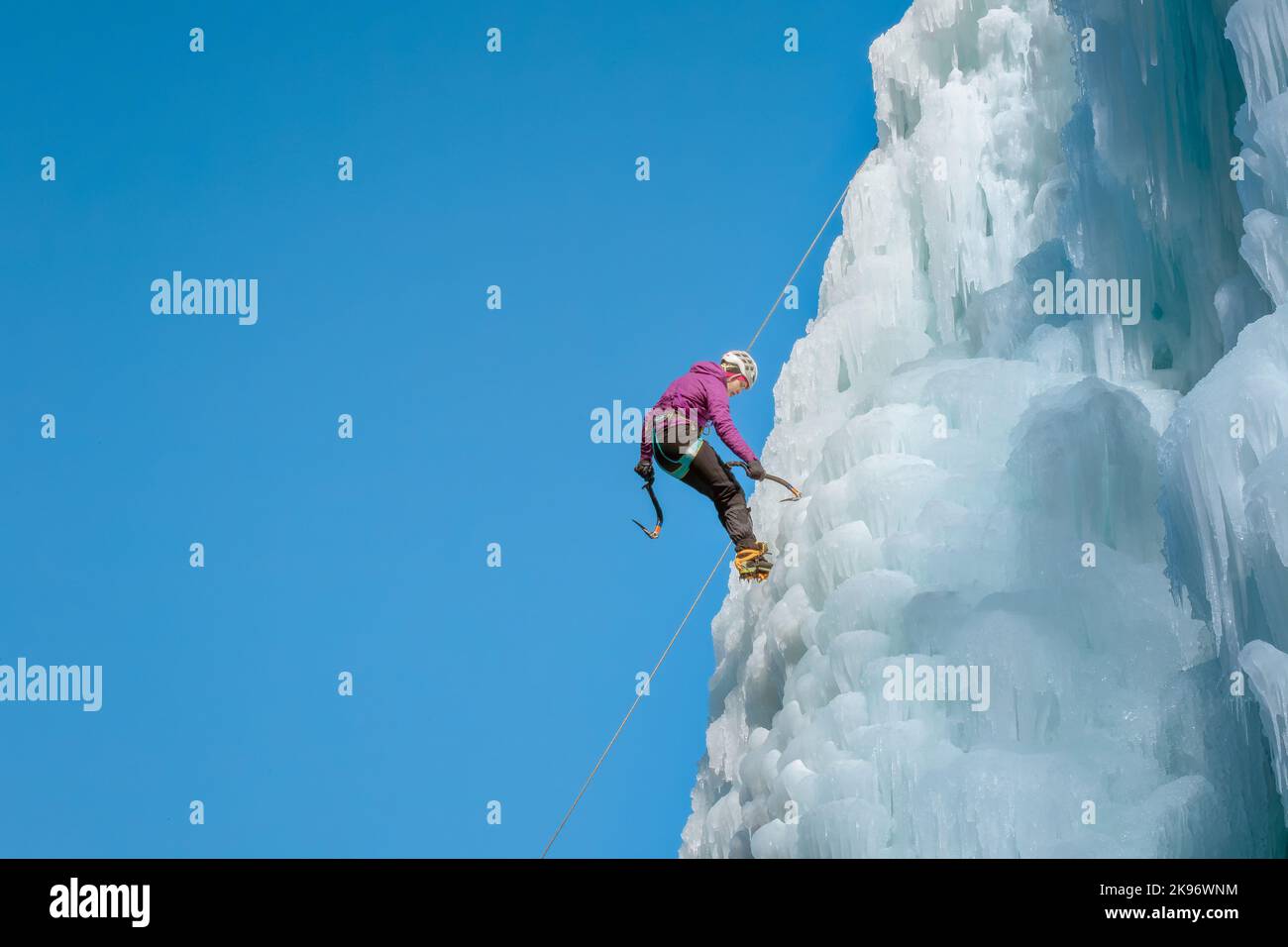 Alpinistin mit Eiskletterausrüstung an einem gefrorenen Wasserfall Stockfoto