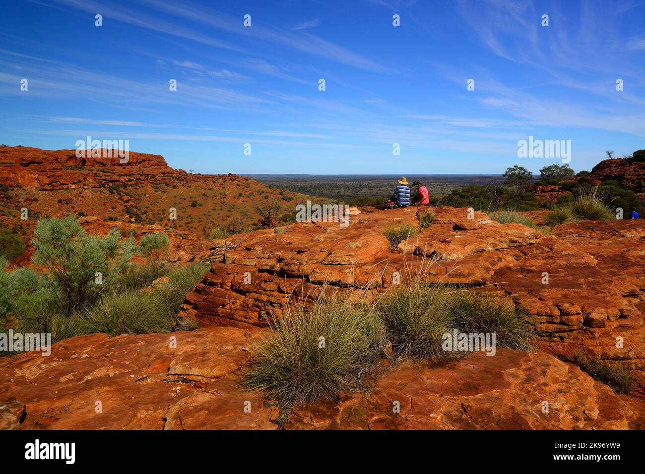Eine lange Aufnahme von zwei Personen, die auf den Olgas, einer Gruppe großer Felsen, im Northern Territory in Australien, mit einem klaren blauen Himmel im Hintergrund sitzen Stockfoto