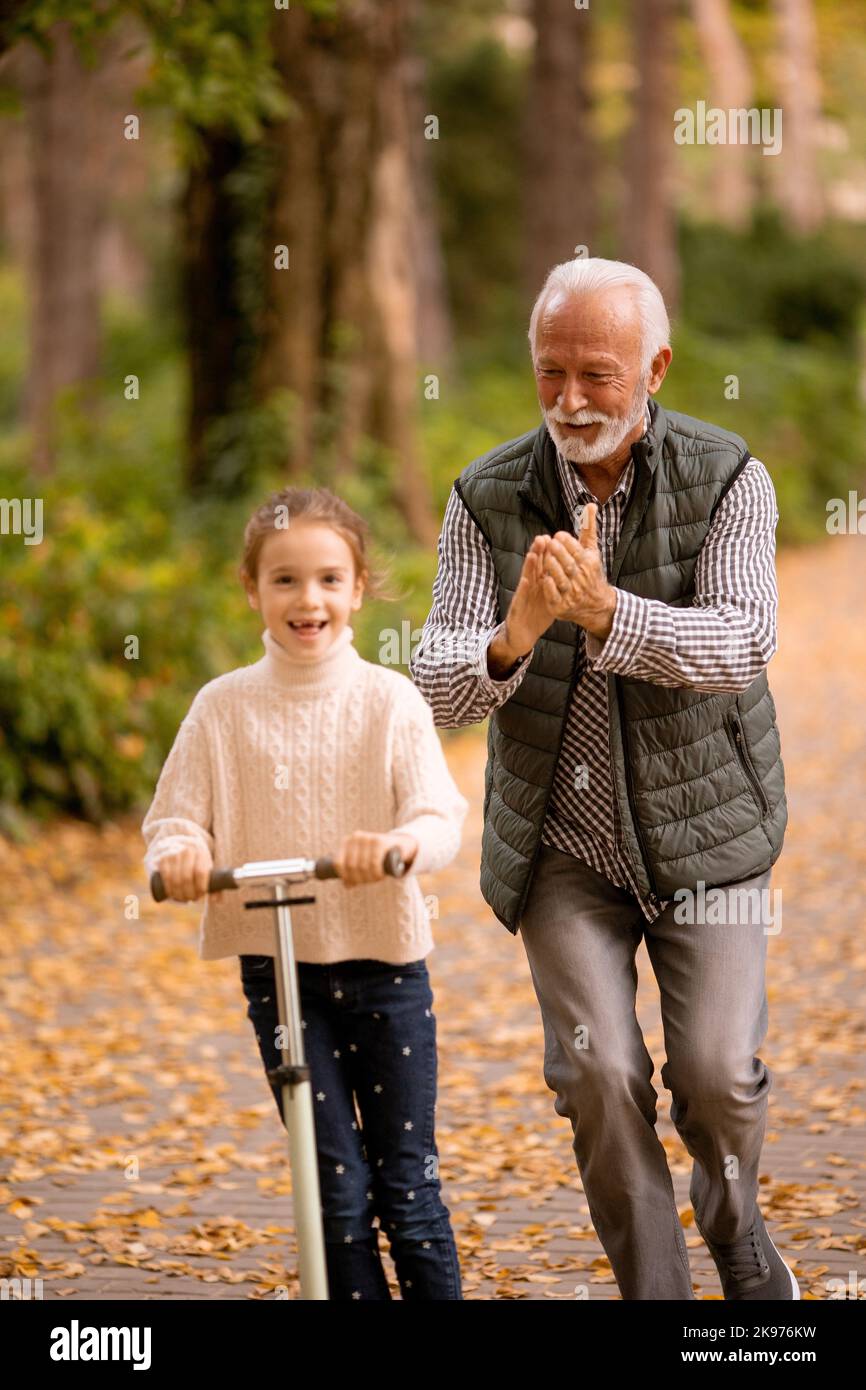 Ein älterer Mann lehrt seine Enkelin, wie man im Herbstpark mit dem Kick Scooter fährt Stockfoto