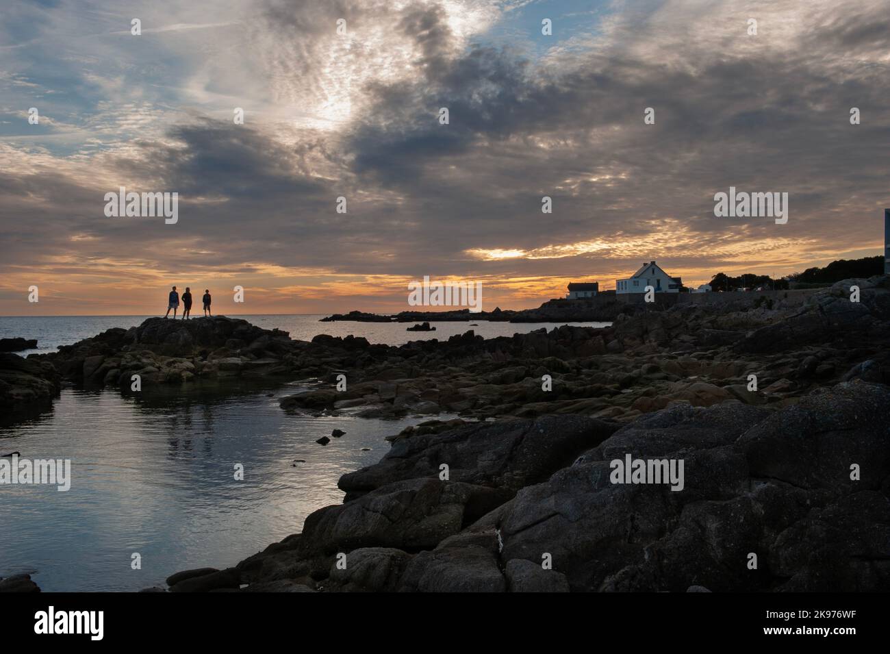 Familie, die auf Felsen steht, die vom Sonnenuntergang abgeschnitten und vor dem dramatischen Himmel und der französischen Küste geschildet werden Stockfoto