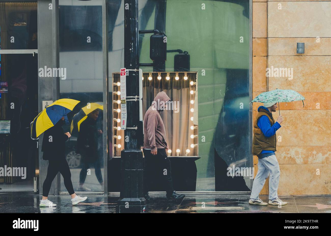 Die drei Menschen, die an einem regnerischen Tag mit Regenschirmen durch die nassen Straßen laufen Stockfoto