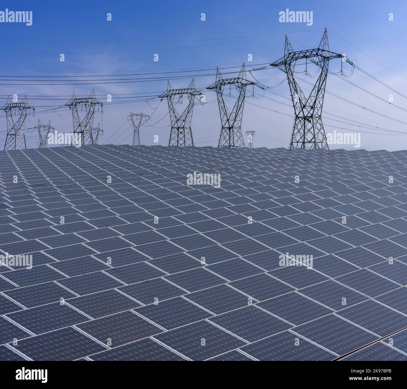 Sonnenkollektoren mit Hochspannungsmasten am blauen Himmel, Elektrizitätsproduktionsanlage mit großer Oberfläche von Sonnenkollektoren Stockfoto