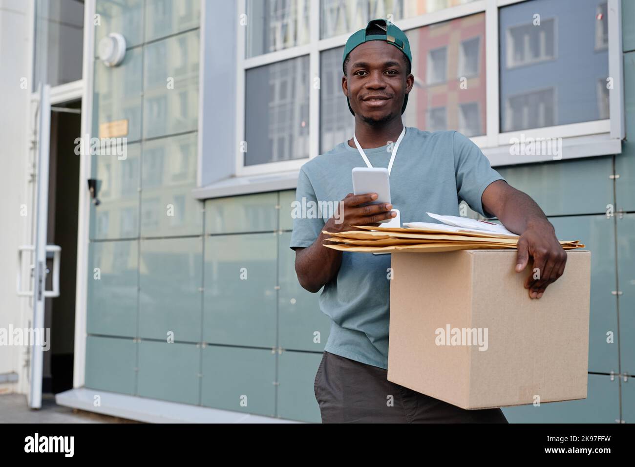 Porträt eines afroamerikanischen Lieferers, der in der City Box hält und die Kamera anlächelt Stockfoto