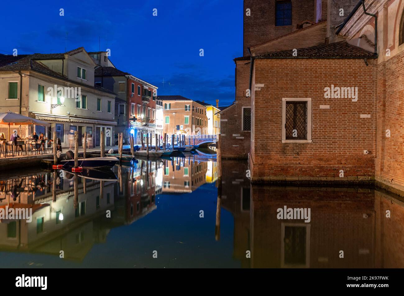 Allgemeiner Blick auf die Kanäle von Chioogia (Spitzname „Klein-Venedig“) mit den Booten und Gebäuden, die sich in der Dämmerung im Wasser unter dem künstlichen Licht spiegeln. Chioggia, eine Stadt in der venezianischen Lagune, die viele Touristen beherbergt, die Venedig besuchen, wurde nicht in den venezianischen Stadtkern aufgenommen. Touristen, die dort bleiben, müssen die Steuer jedes Mal zahlen, wenn sie Venedig ab dem 16. Januar 2023 besuchen. Stockfoto