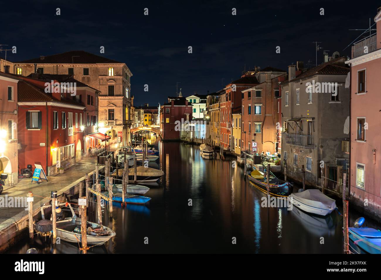 Allgemeiner Blick auf die Kanäle von Chioogia (Spitzname „Klein-Venedig“) mit den Booten und Gebäuden, die sich in der Dämmerung im Wasser unter dem künstlichen Licht spiegeln. Chioggia, eine Stadt in der venezianischen Lagune, die viele Touristen beherbergt, die Venedig besuchen, wurde nicht in den venezianischen Stadtkern aufgenommen. Touristen, die dort bleiben, müssen die Steuer jedes Mal zahlen, wenn sie Venedig ab dem 16. Januar 2023 besuchen. Stockfoto