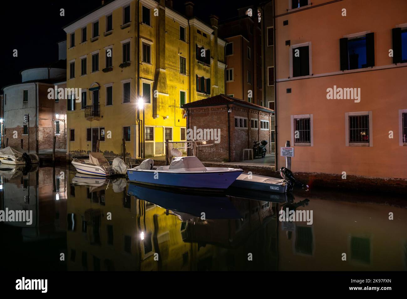 Allgemeiner Blick auf die Kanäle von Chioogia (Spitzname „Klein-Venedig“) mit den Booten und Gebäuden, die sich in der Dämmerung im Wasser unter dem künstlichen Licht spiegeln. Chioggia, eine Stadt in der venezianischen Lagune, die viele Touristen beherbergt, die Venedig besuchen, wurde nicht in den venezianischen Stadtkern aufgenommen. Touristen, die dort bleiben, müssen die Steuer jedes Mal zahlen, wenn sie Venedig ab dem 16. Januar 2023 besuchen. Stockfoto