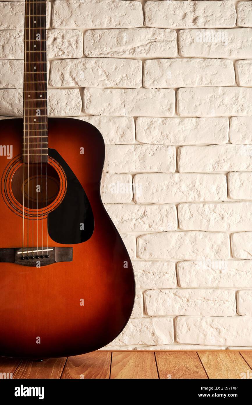 Vertikale Kulisse mit einer Akustikgitarre auf dem Holzboden in der Nähe der Backsteinmauer. Musik und Hobby Konzept Hintergrund. Platz für Text kopieren Stockfoto