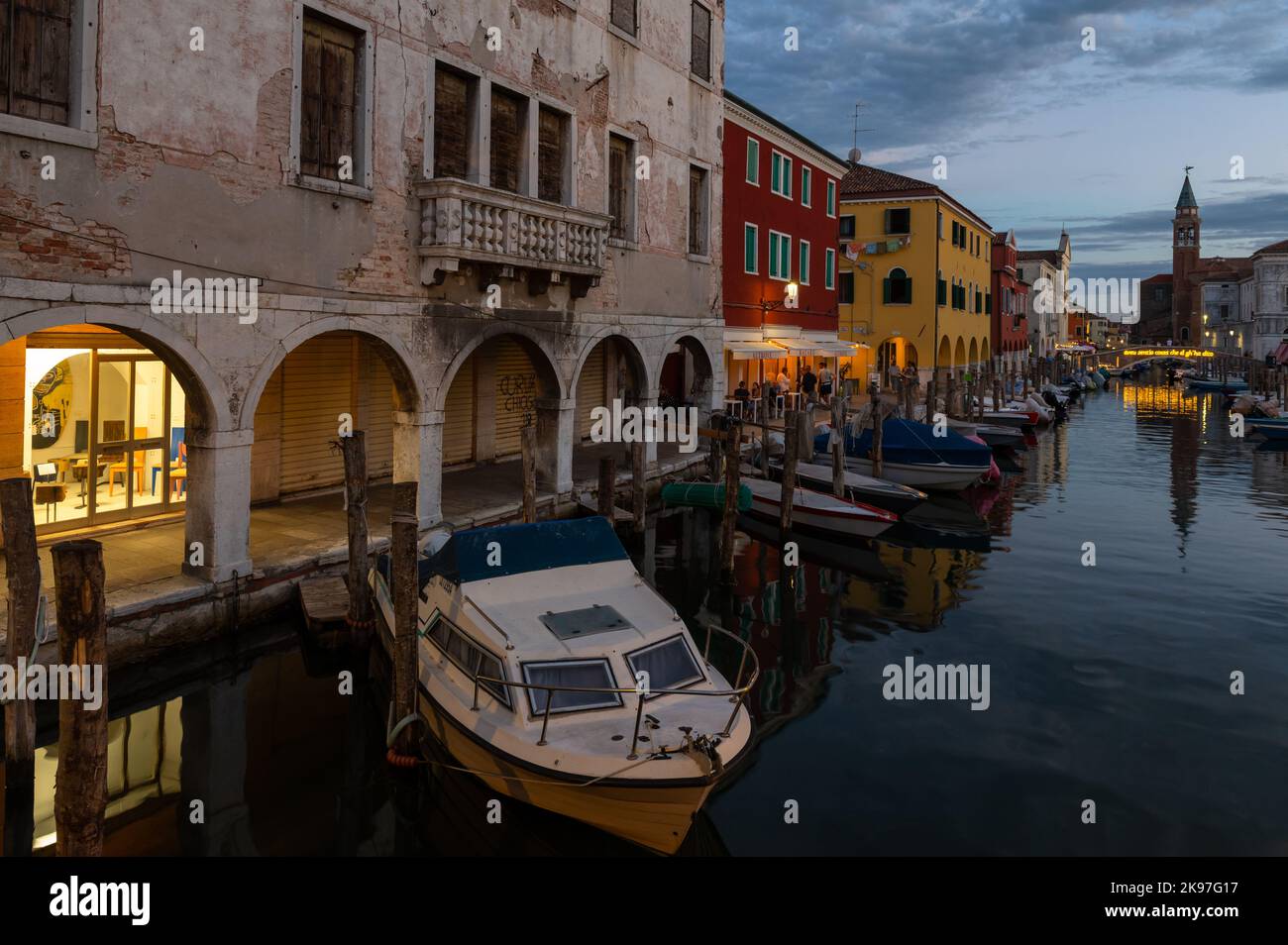 Allgemeiner Blick auf die Kanäle von Chioogia (Spitzname „Klein-Venedig“) mit den Booten und Gebäuden, die sich in der Dämmerung im Wasser unter dem künstlichen Licht spiegeln. Chioggia, eine Stadt in der venezianischen Lagune, die viele Touristen beherbergt, die Venedig besuchen, wurde nicht in den venezianischen Stadtkern aufgenommen. Touristen, die dort bleiben, müssen die Steuer jedes Mal zahlen, wenn sie Venedig ab dem 16. Januar 2023 besuchen. Stockfoto