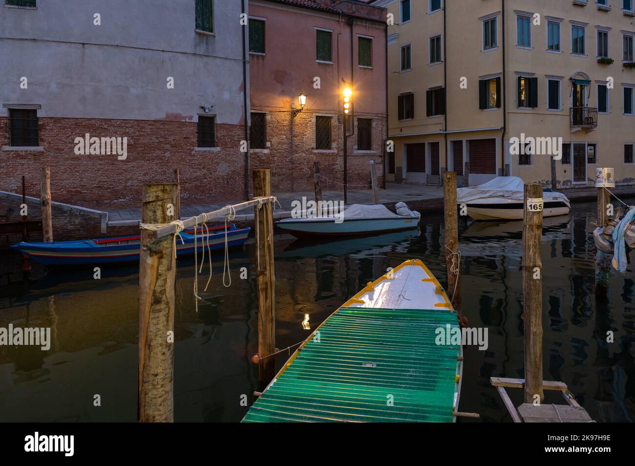 Chioggia, Italien. 20. August 2022. Allgemeiner Blick auf die Kanäle von Chioogia (Spitzname „Klein-Venedig“) mit den Booten und Gebäuden, die sich in der Dämmerung im Wasser unter dem künstlichen Licht spiegeln. Chioggia, eine Stadt in der venezianischen Lagune, die viele Touristen beherbergt, die Venedig besuchen, wurde nicht in den venezianischen Stadtkern aufgenommen. Touristen, die dort bleiben, müssen die Steuer jedes Mal zahlen, wenn sie Venedig ab dem 16. Januar 2023 besuchen. (Foto: Laurent Coust/SOPA Images/Sipa USA) Quelle: SIPA USA/Alamy Live News Stockfoto