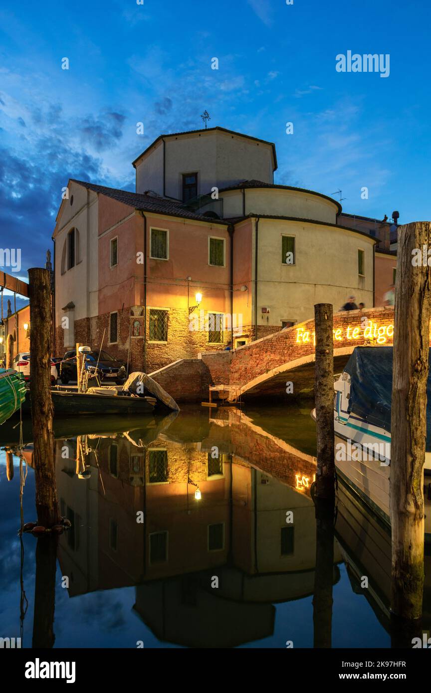 Chioggia, Italien. 20. August 2022. Allgemeiner Blick auf die Kanäle von Chioogia (Spitzname „Klein-Venedig“) mit den Booten und Gebäuden, die sich in der Dämmerung im Wasser unter dem künstlichen Licht spiegeln. Chioggia, eine Stadt in der venezianischen Lagune, die viele Touristen beherbergt, die Venedig besuchen, wurde nicht in den venezianischen Stadtkern aufgenommen. Touristen, die dort bleiben, müssen die Steuer jedes Mal zahlen, wenn sie Venedig ab dem 16. Januar 2023 besuchen. (Foto: Laurent Coust/SOPA Images/Sipa USA) Quelle: SIPA USA/Alamy Live News Stockfoto