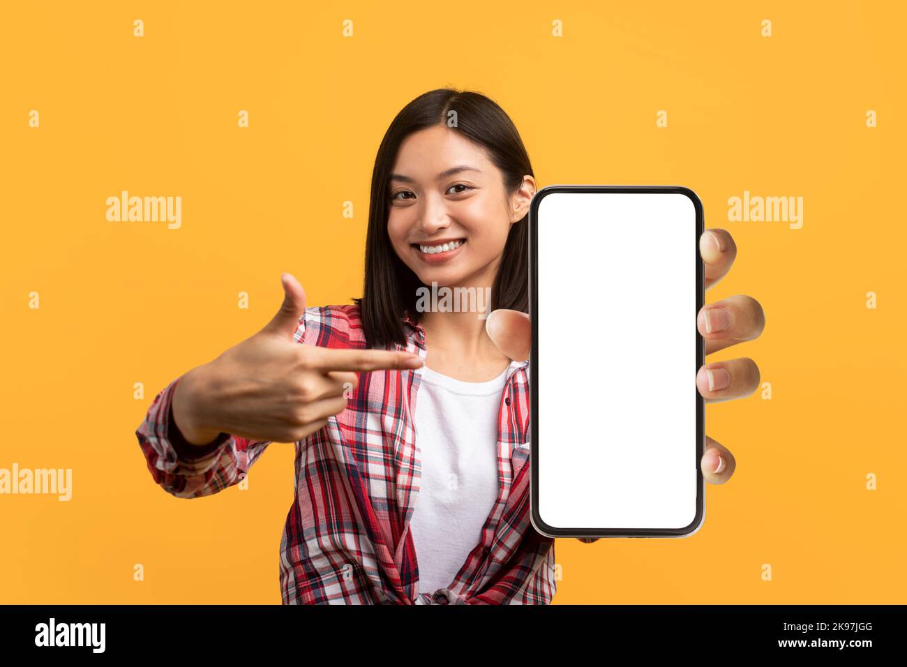 Tolle mobile App. Positive asiatische Dame zeigt auf Handy mit leerem Bildschirm, bietet Platz für Anzeige, mockup Stockfoto
