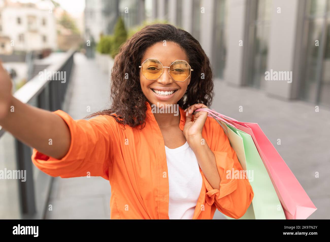 Happy Millennial african american Lady in Casual und Brille mit vielen Taschen genießt zu Fuß und nimmt Selfie Stockfoto
