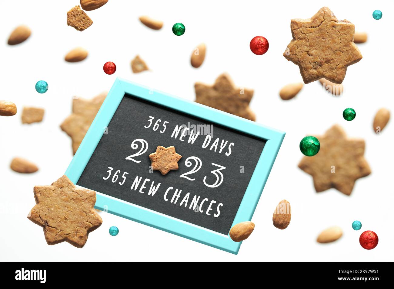 Neujahr 2023, 365 neue Tage, 365 neue Chancen Text. Schweben von Sternkeksen und Schokoladenkugeln in Folie, die um Kreidetafel mit Gruß fliegen Stockfoto