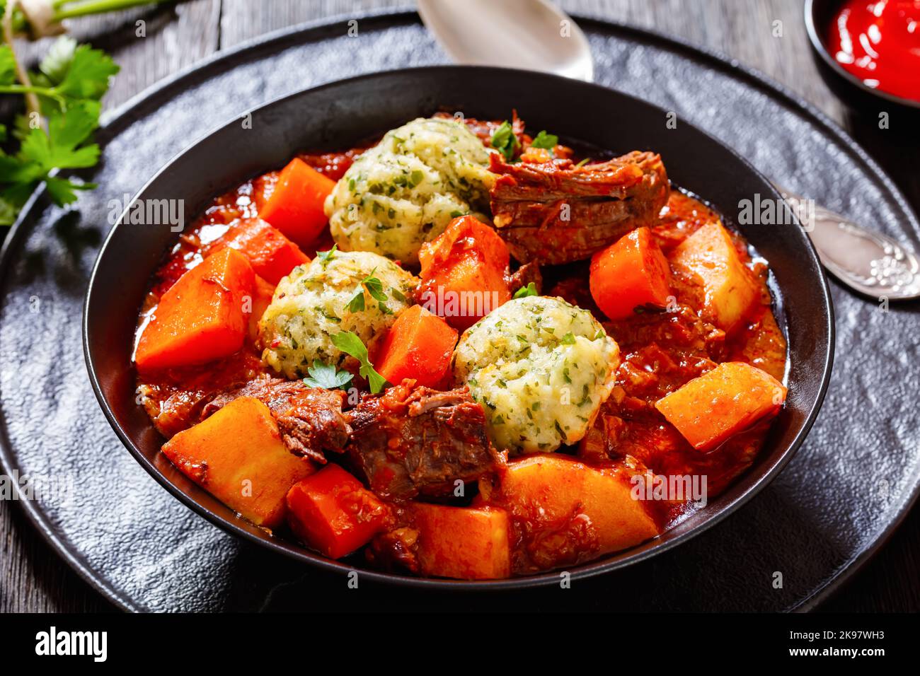 Rindereintopf mit Knödeln und Gemüse in reicher Tomate und Soße auf Brühe in schwarzer Schüssel, britische Küche, Nahaufnahme Stockfoto