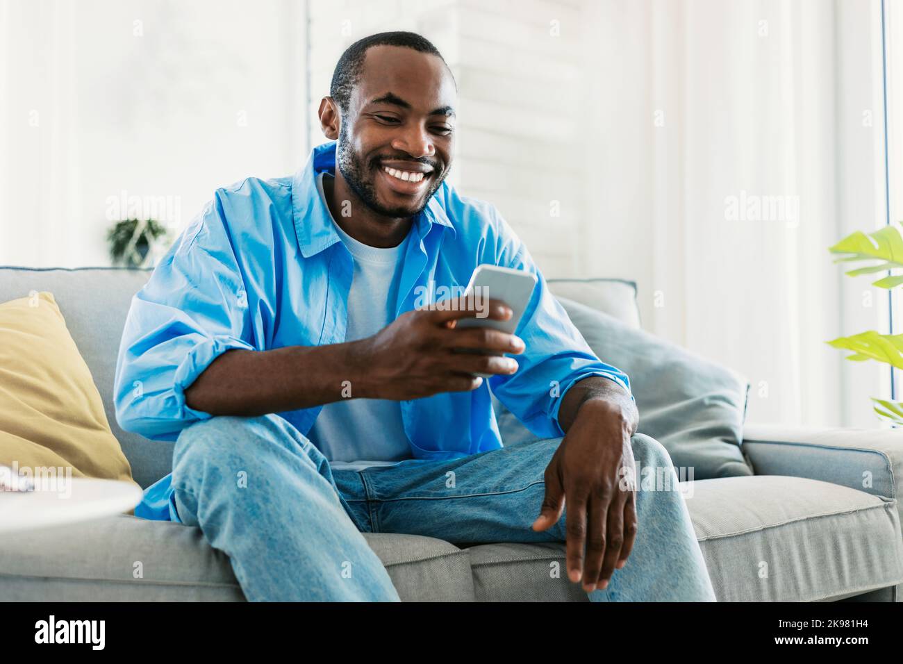 Cooles Gadget- und App-Konzept. Porträt eines glücklichen schwarzen Mannes, der mit dem Mobiltelefon unterwegs war, Videos ansah, auf dem Sofa saß und Platz für Kopien benutzte Stockfoto